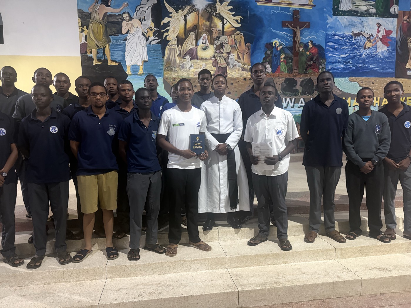 Aman Lyimo with a group of students at the parish, holding a copy of Now I Know