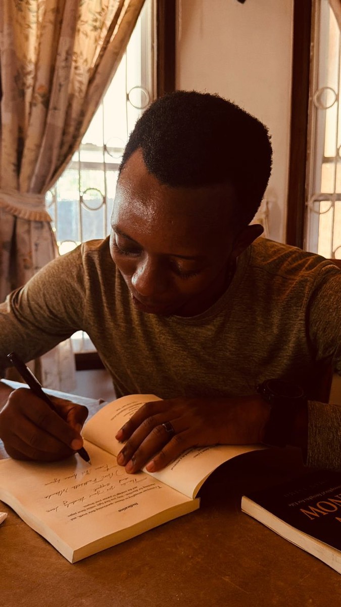 Aman Lyimo signing a copy of Now I Know at a table